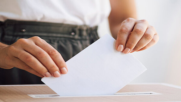 A person putting a ballot paper into a ballot box