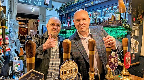 Cameron stands behind a bar pouring a pint